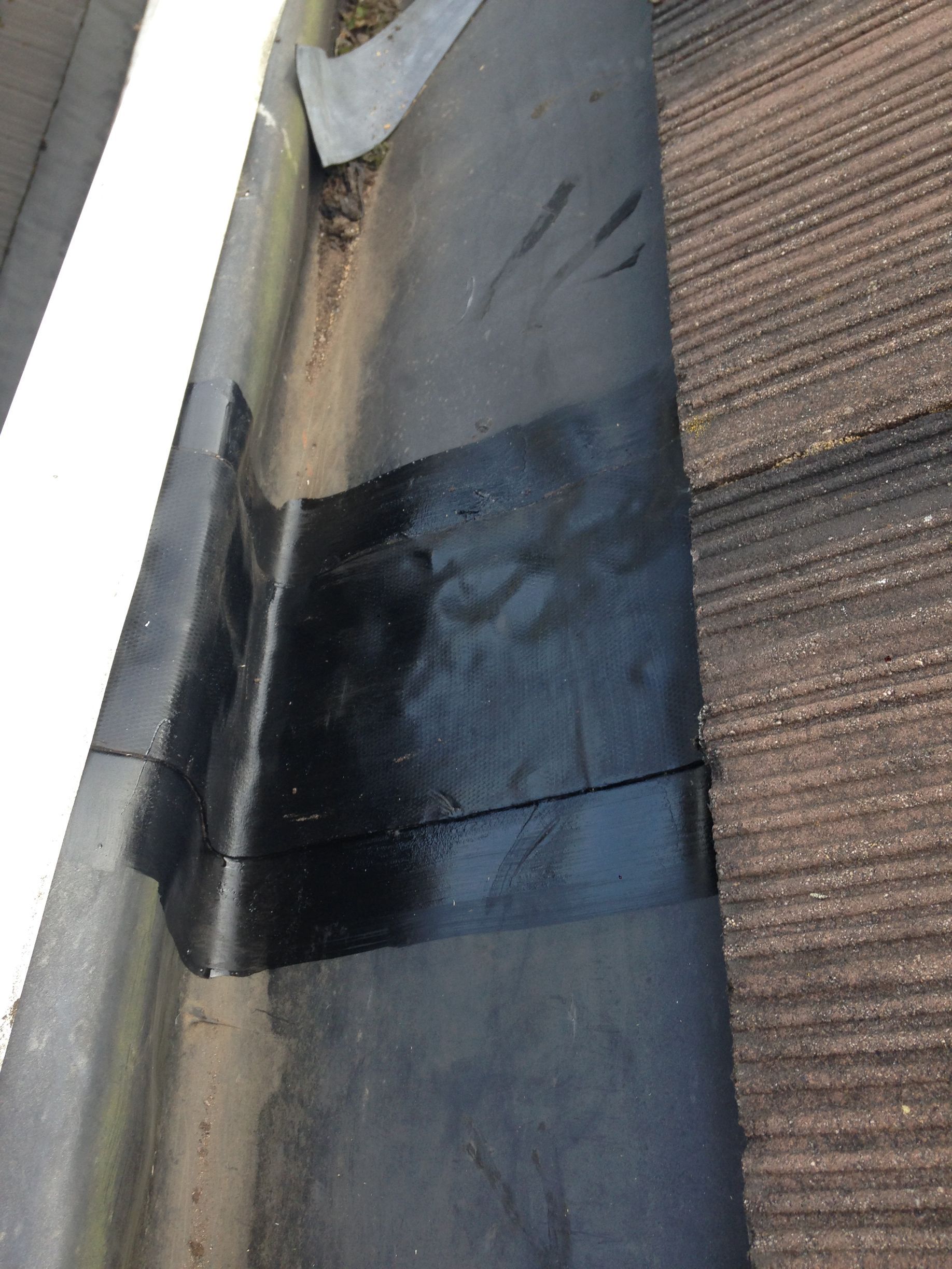 A close up of a gutter on a roof with water coming out of it.
