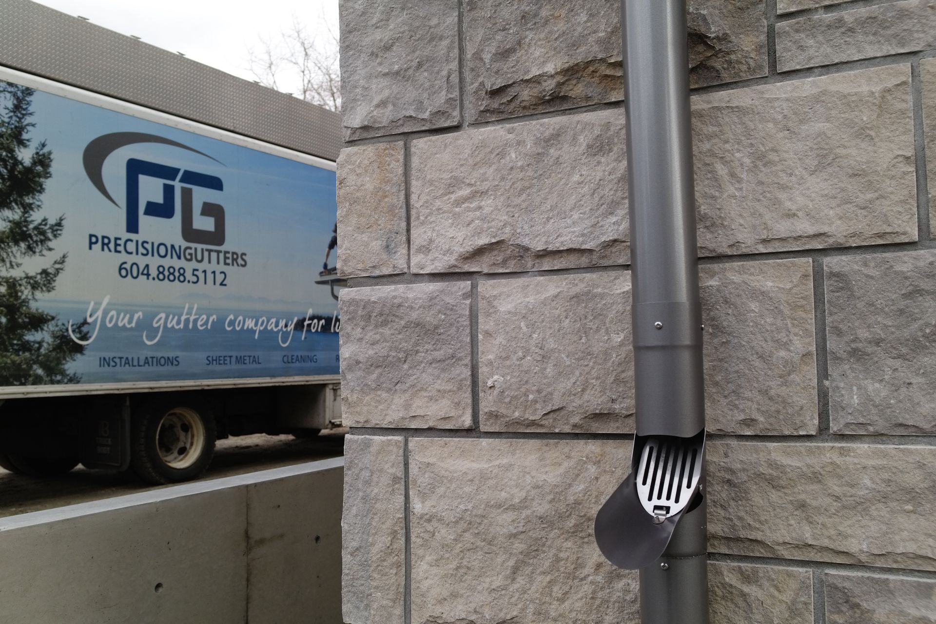 A truck is parked in front of a brick wall next to a drain pipe.
