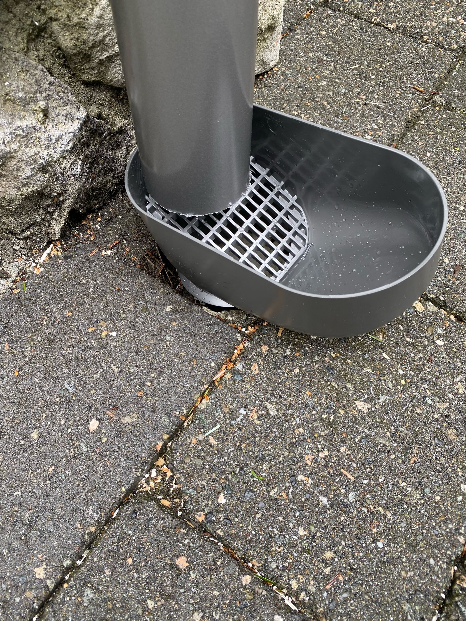 A gray cat litter scoop is sitting on a brick sidewalk.
