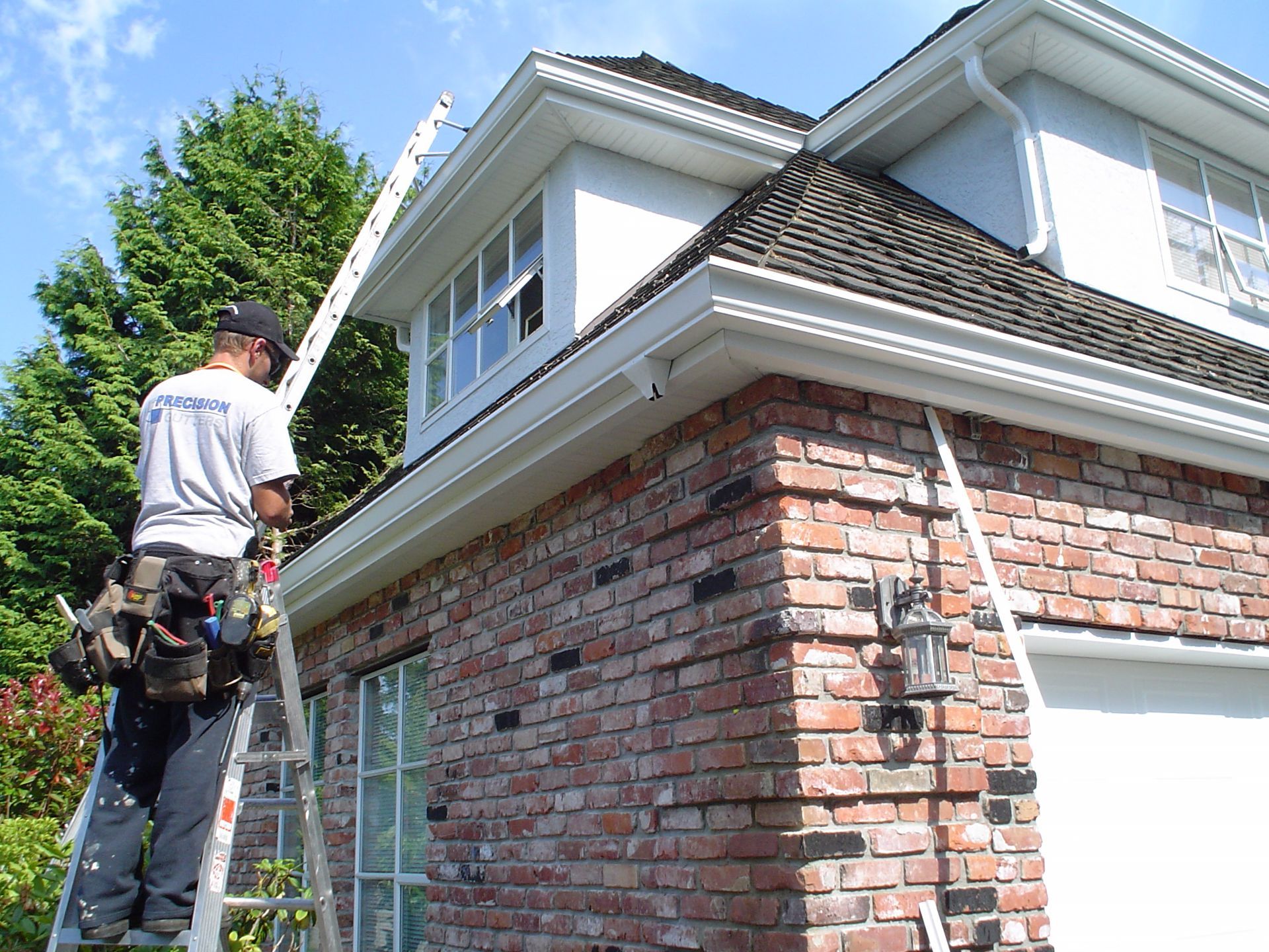 A man on a ladder is working on the roof of a brick house