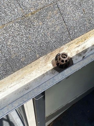 A close up of a drain on a roof next to a window.