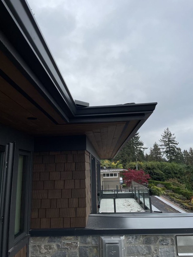 The roof of a house with a balcony and trees in the background.