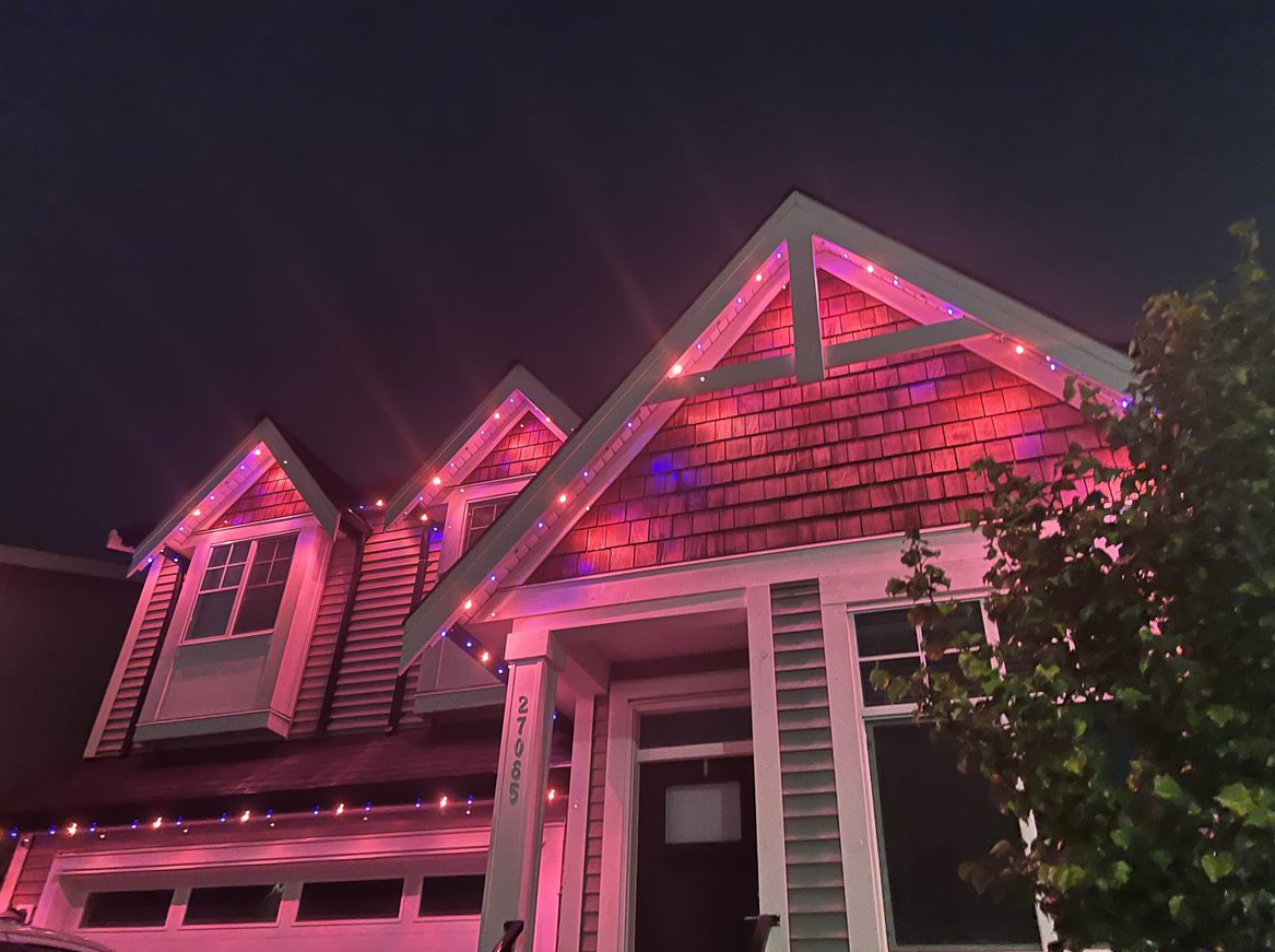 A house is decorated with pink christmas lights at night.