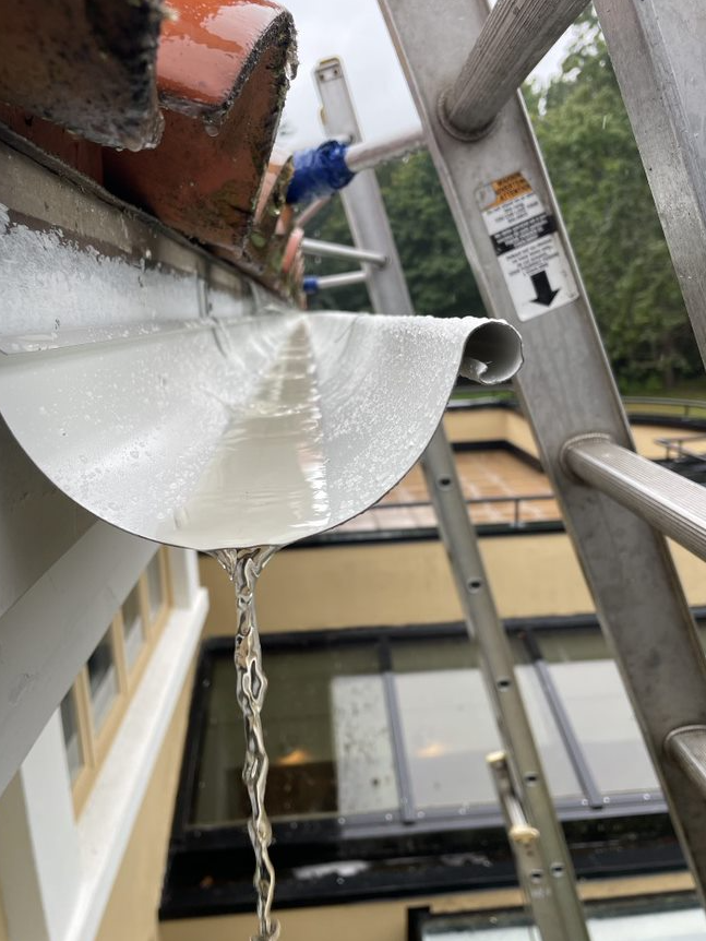 A gutter with water coming out of it next to a ladder
