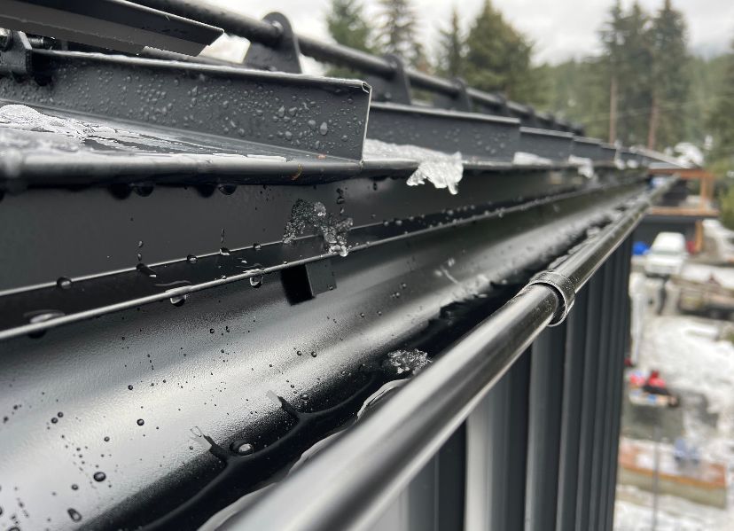 A close up of a black gutter on a roof with snow on it.