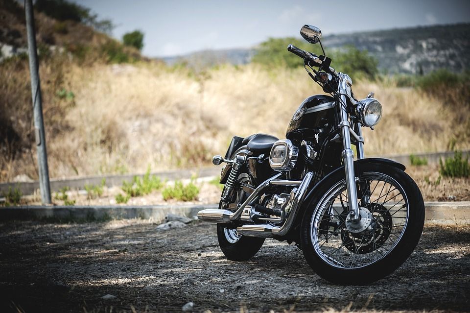 Black motorcycle parked on a dirt road with tall grass and hills in the background
