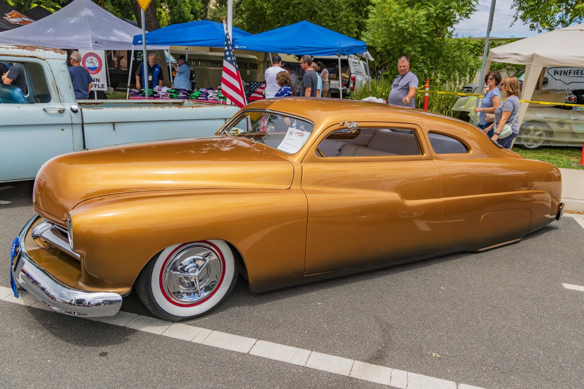 Copper vintage custom car at an outdoor car show, with tents and people in the background