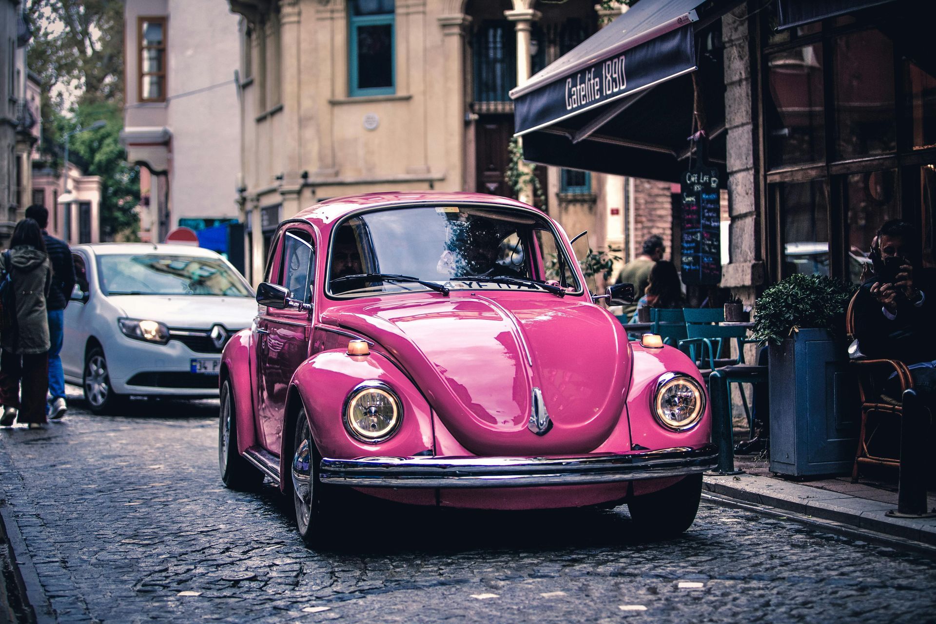 Pink vintage Volkswagen Beetle driving on a cobblestone street in a European town