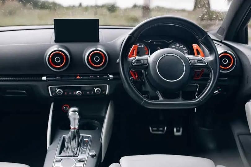 Modern car interior with black dashboard, red-accented circular vents, steering wheel, and center console
