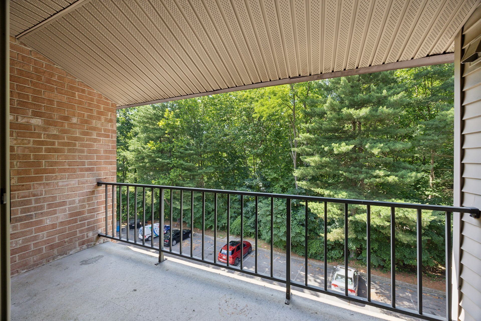 Balcony overlooking street and trees, black railing, brick wall on the left, white siding on the right.