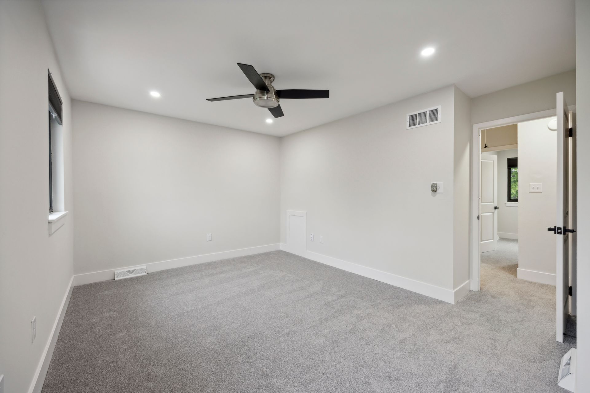 Empty bedroom with gray carpet, white walls, ceiling fan, and open doorway.