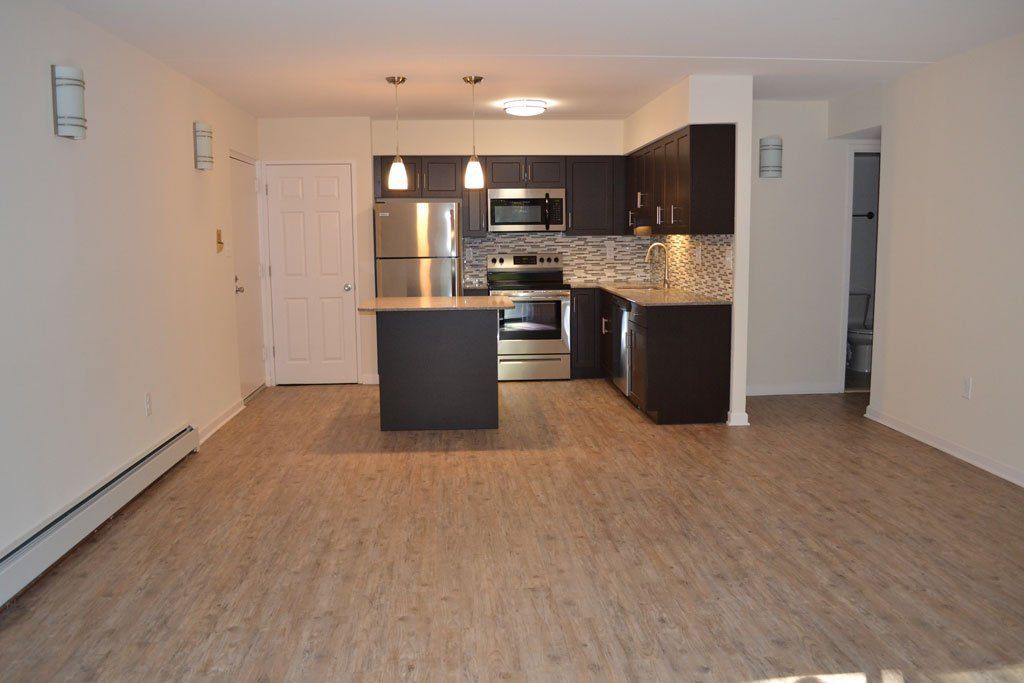 Open-plan kitchen and living area with wood flooring, dark cabinetry, and stainless steel appliances.