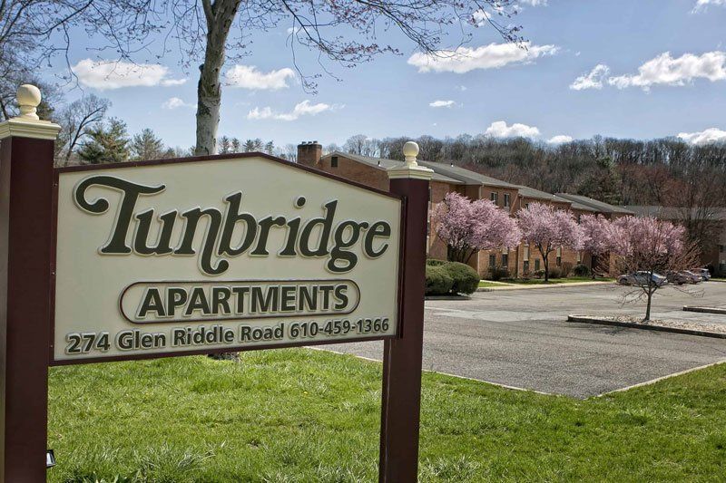 Sign for Tunbridge Apartments, with building and cherry trees in the background. Green grass and blue sky.