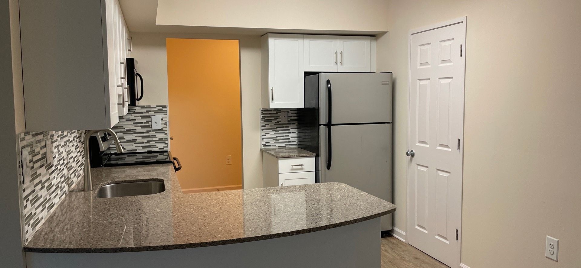 Kitchen with countertop, stove, stainless steel refrigerator, white cabinets, and an orange door.