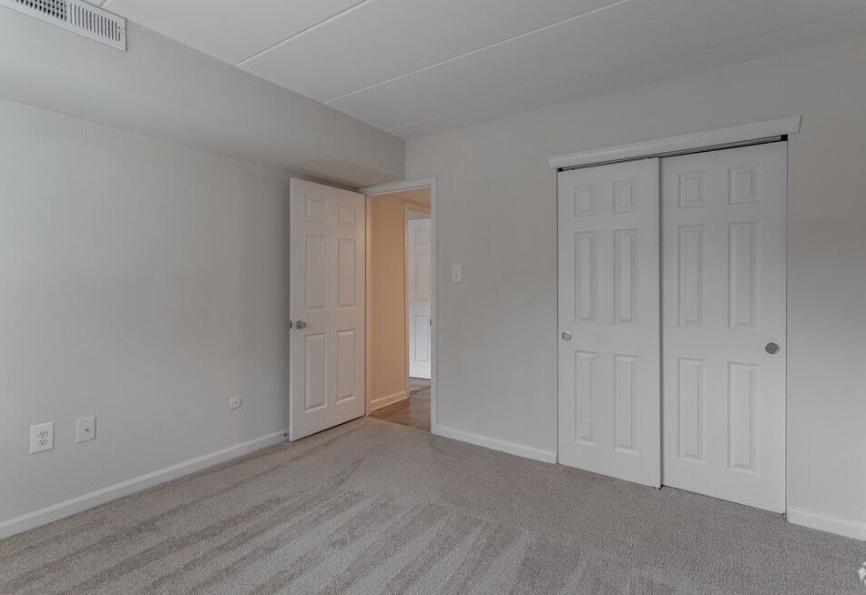 Empty bedroom with gray carpet, white walls, two closet doors, and a doorway.