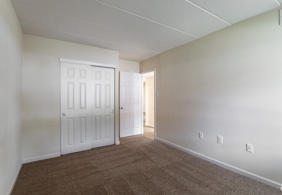 Empty bedroom with beige walls, brown carpet, and two white doors.