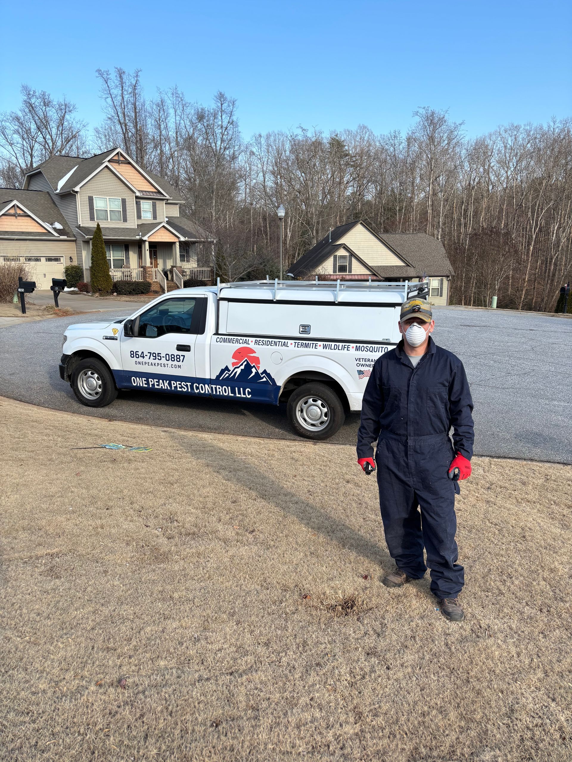 Masked worker standing beside a service truck in a suburban driveway under a clear sky