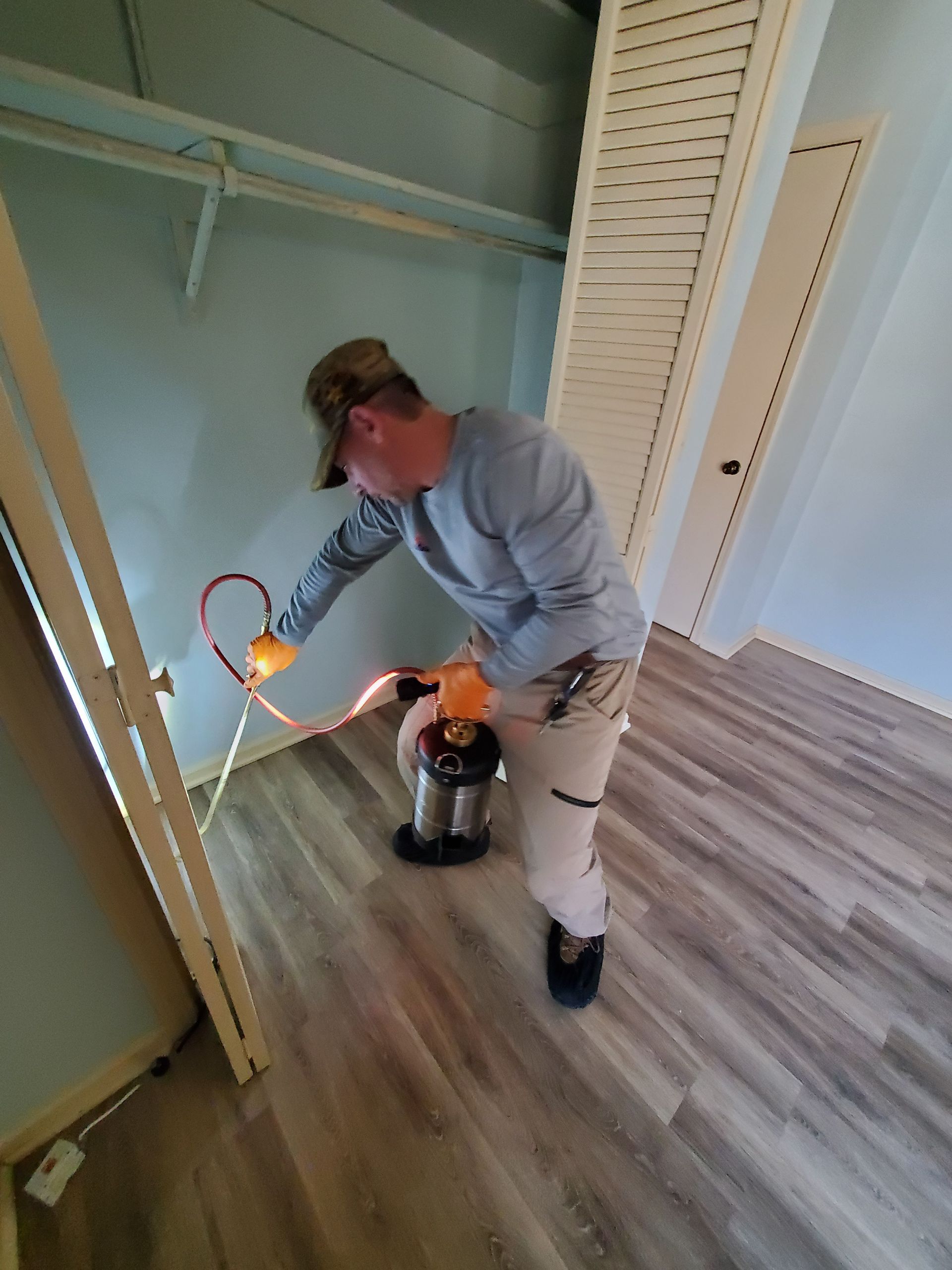 Person using a vacuum in a hallway beside an open closet, with a bright light on the floor.