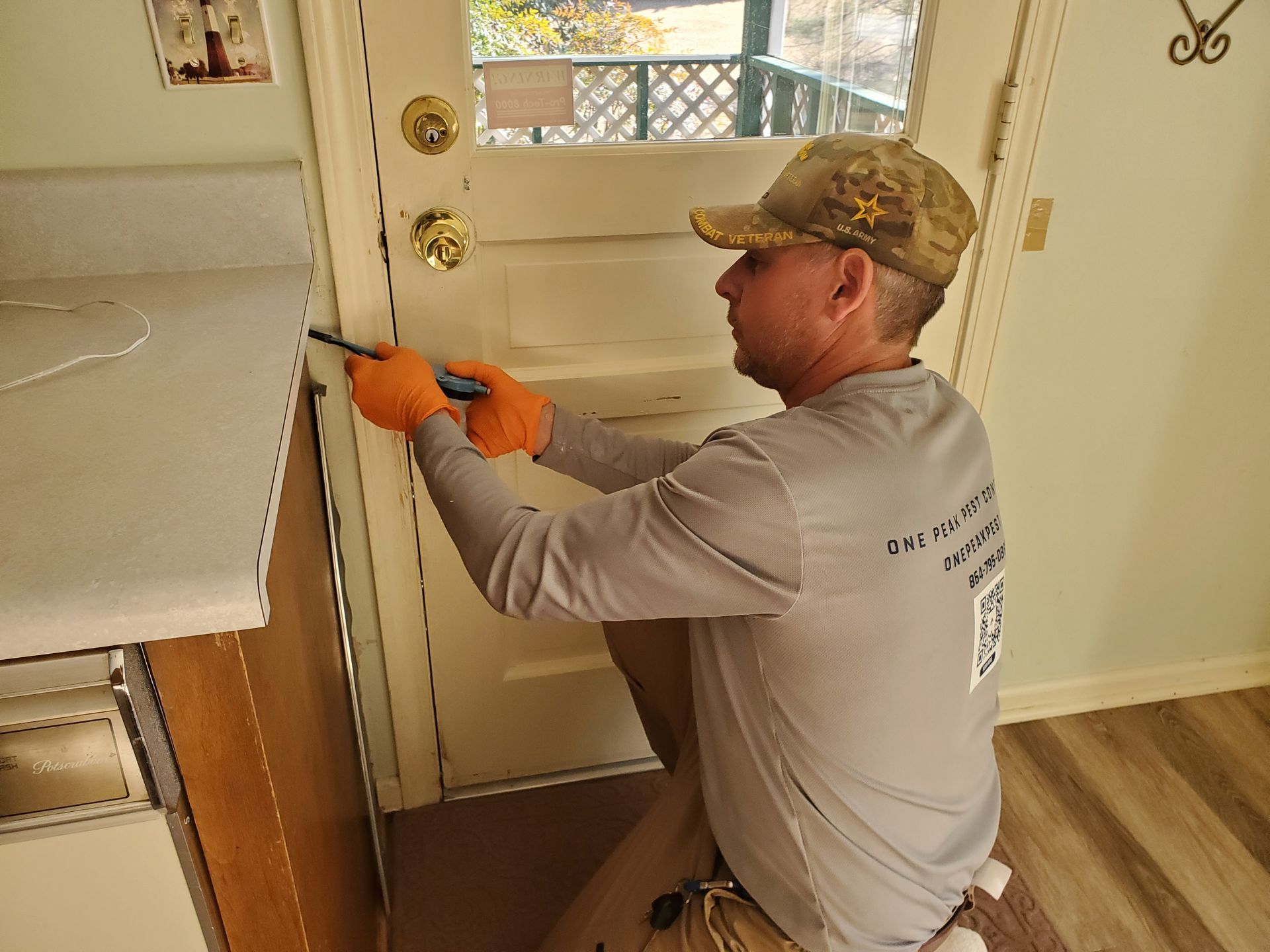 Person kneeling to install a white door latch with a screwdriver in a home kitchen.