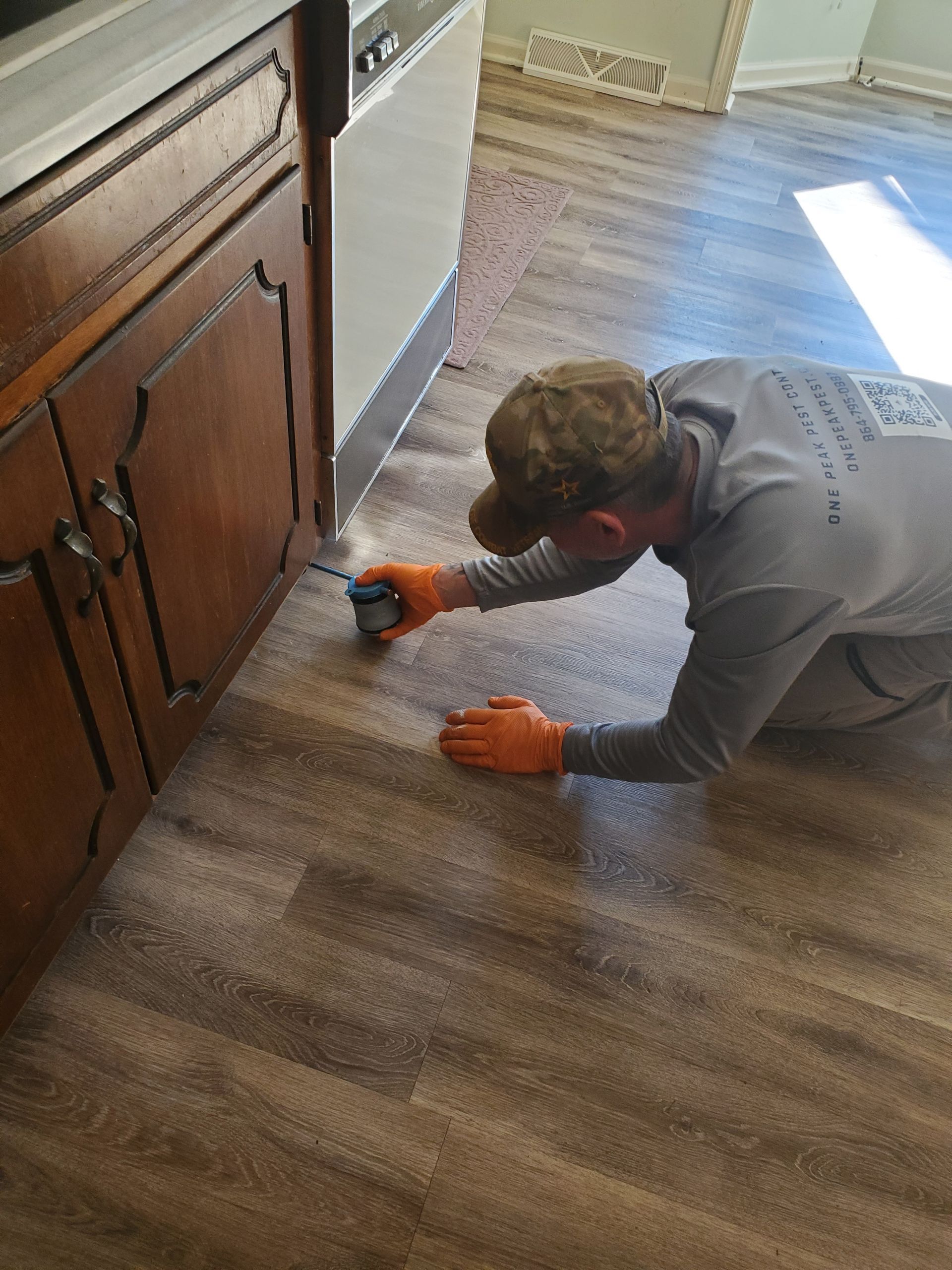Person in orange gloves cleaning a wood floor beside kitchen cabinets with a vacuum attachment