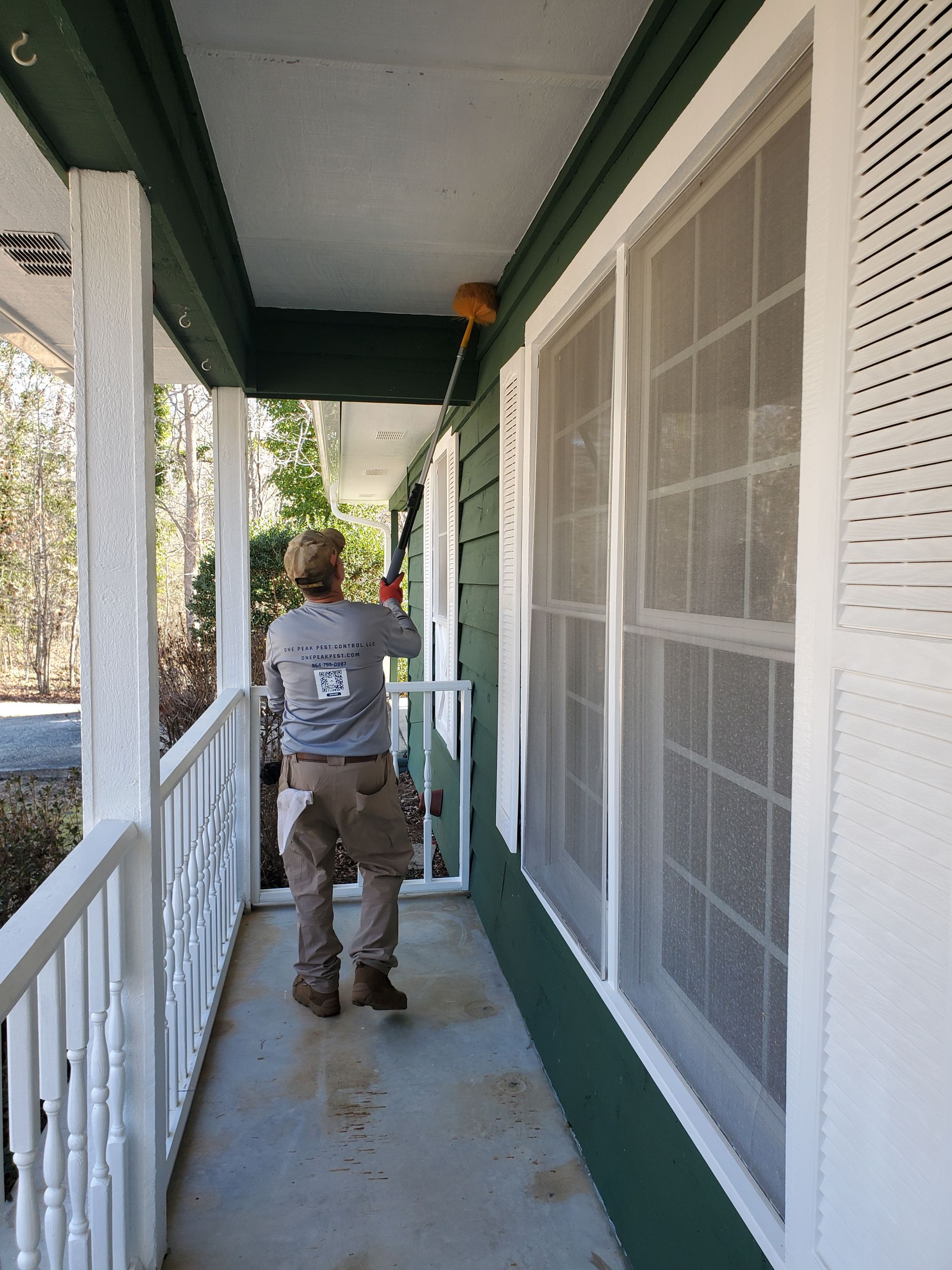 Person walking down a narrow porch with green trim and white railings beside screened windows.