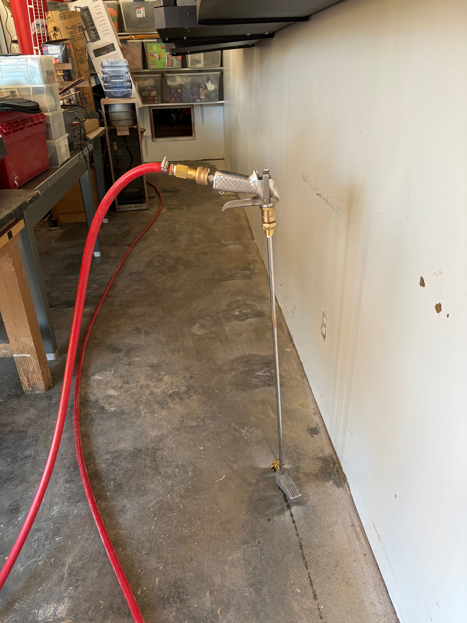 Red hose connected to a wall faucet in a narrow utility hallway, with water draining along the floor.