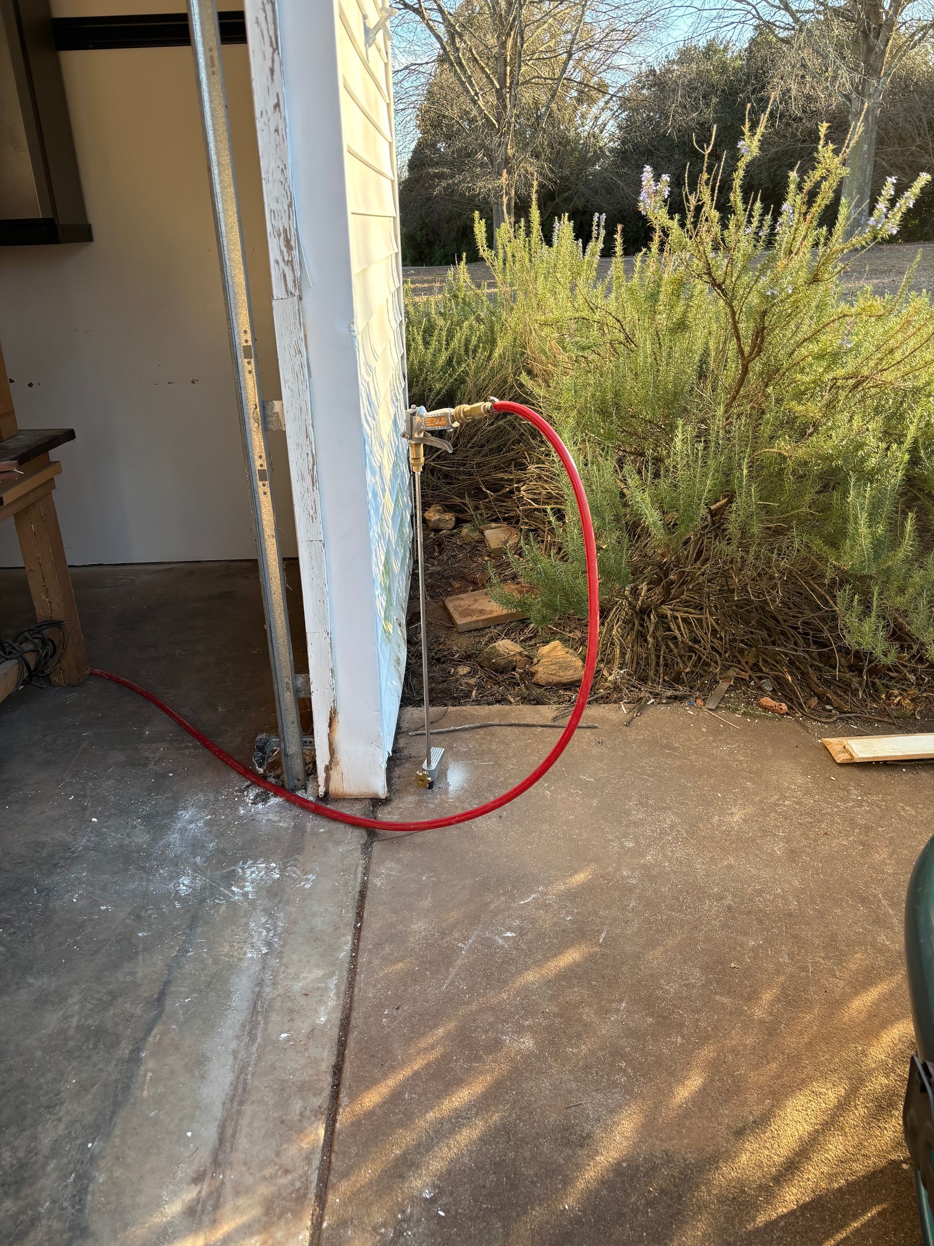 Red hose looped around a doorway edge beside a concrete patio and dry shrubbery.
