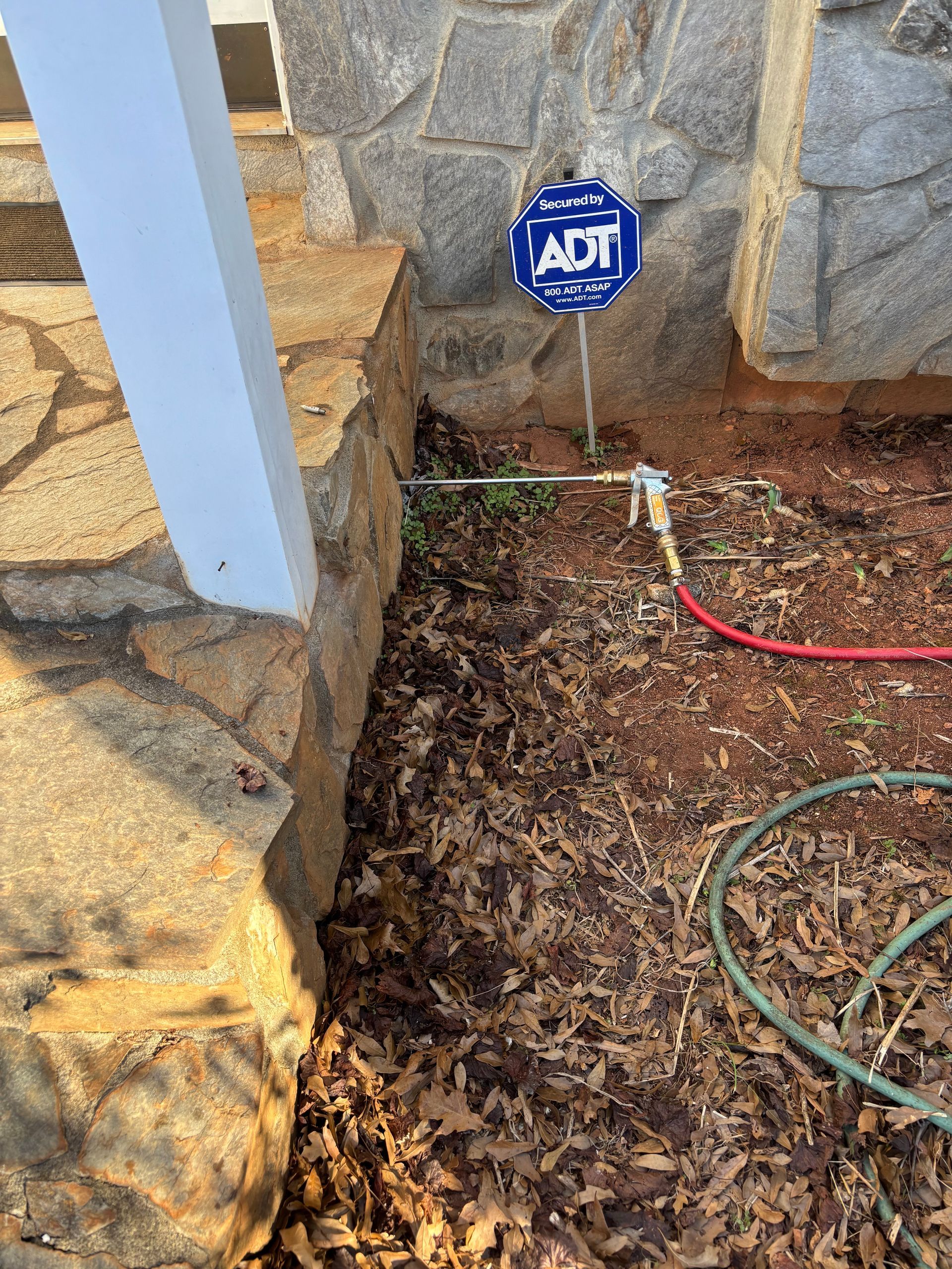 ADT alarm sign in a landscaped yard beside stone steps, with hoses and a white post.