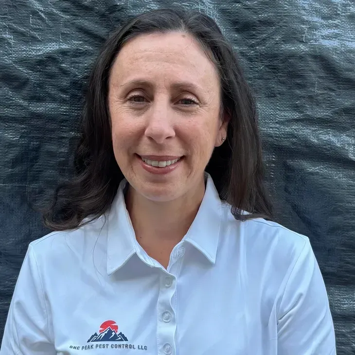 Woman in a white shirt with a company logo smiles in front of a dark backdrop.