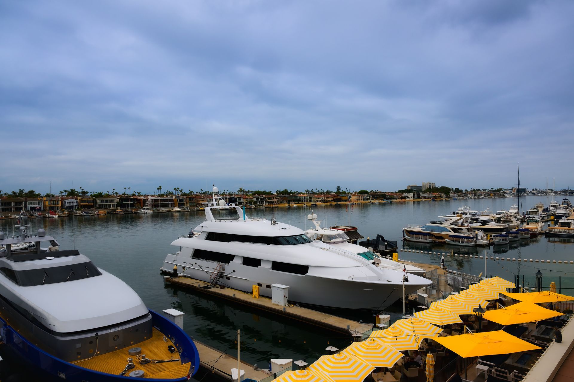 Yachts docked at a marina under a cloudy sky, with yellow floating docks in the foreground