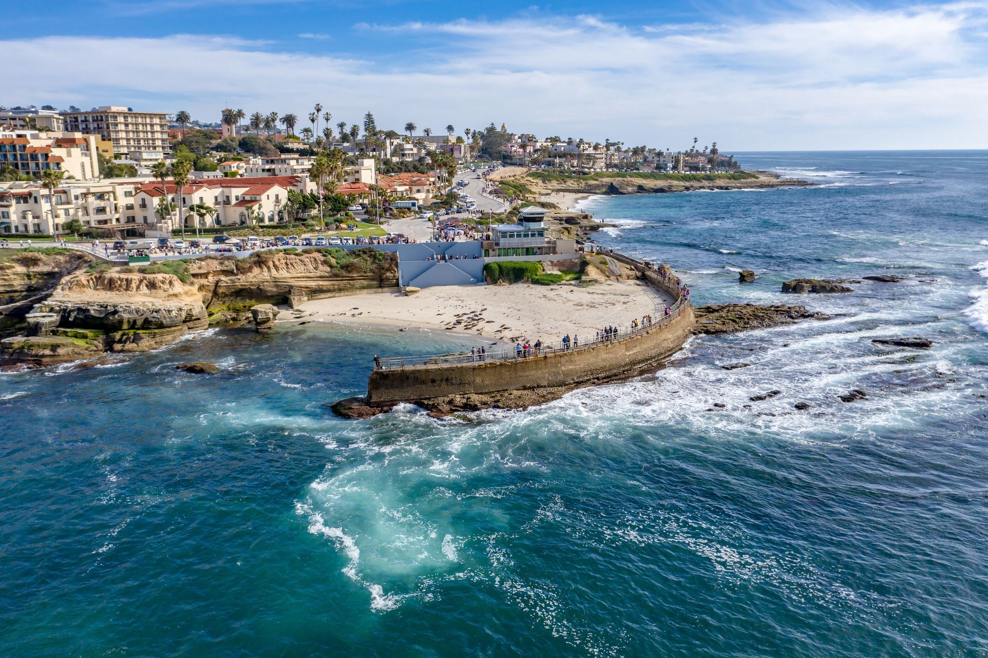Coastal ocean cove with turquoise water, rocky shoreline, and houses along the cliffside under a blue sky Coastal ocean cove with turquoise water, rocky shoreline, and houses along the cliffside under a blue sky