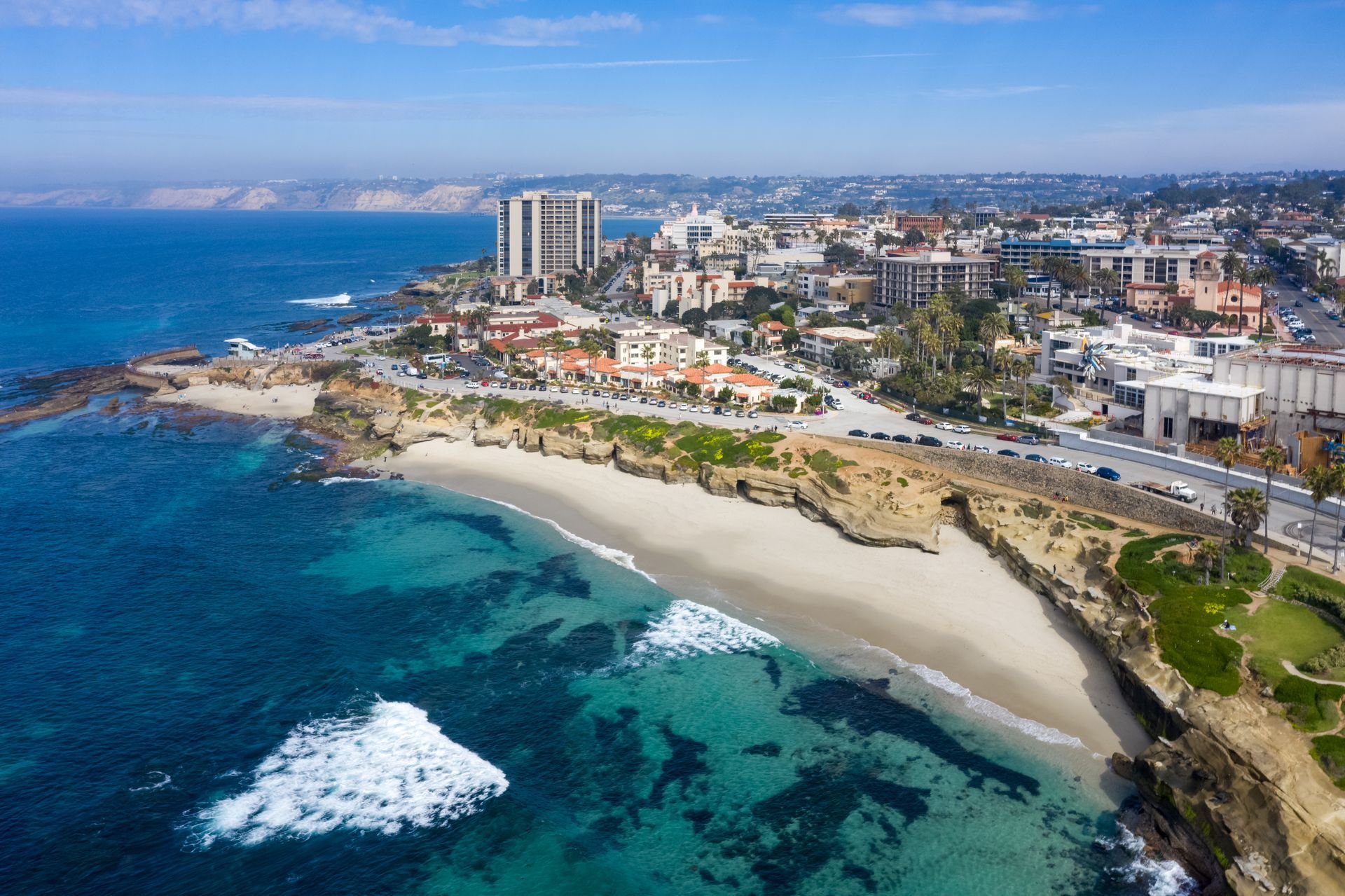 Aerial view of a coastal city with a curved white-sand beach and turquoise ocean
