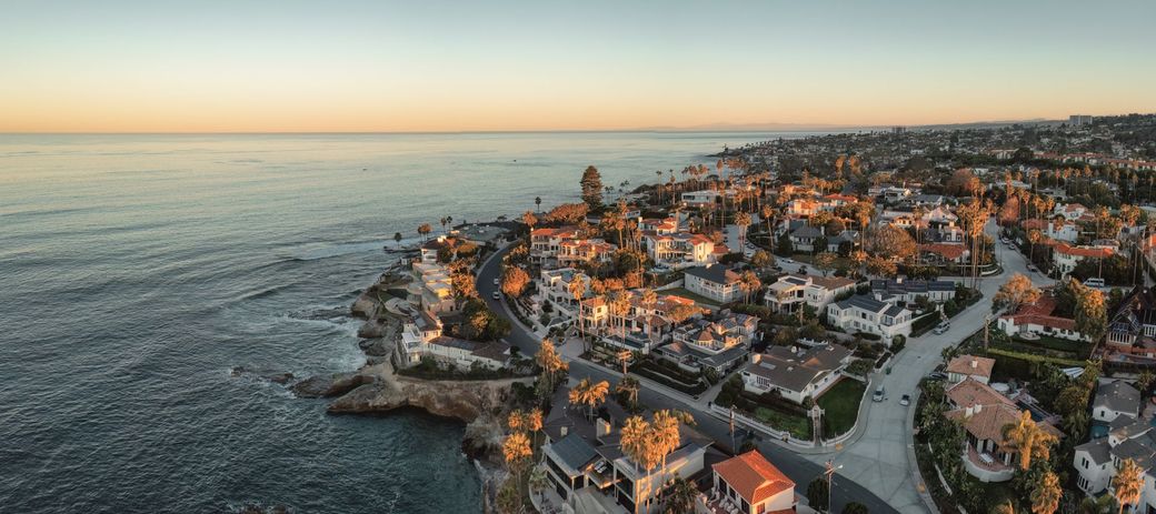 Aerial view of a coastal town at sunset, with ocean, cliffs, and dense seaside buildings. Aerial view of a coastal town at sunset, with ocean, cliffs, and dense seaside buildings.