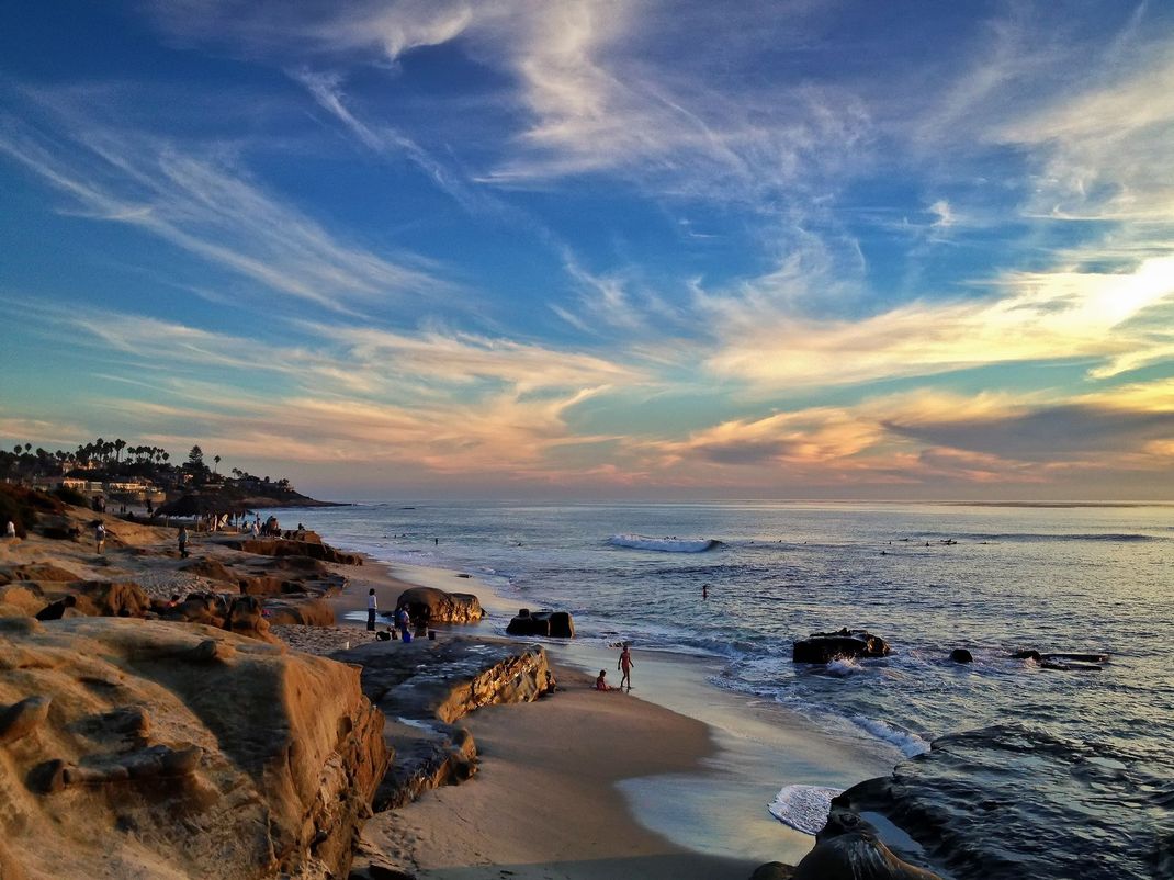 Rocky coastline at sunset with waves, sandy beach, and colorful clouds over the ocean Rocky coastline at sunset with waves, sandy beach, and colorful clouds over the ocean