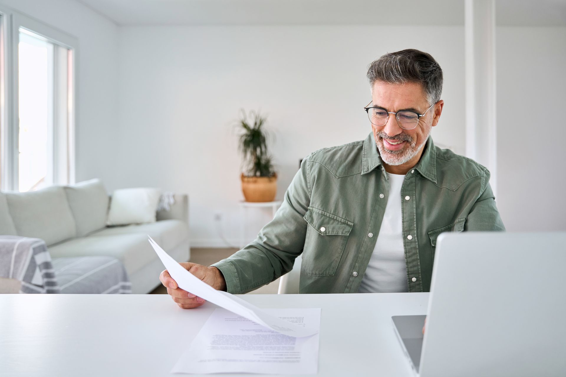 Two people in a meeting, one holding papers across a laptop on a wooden table
