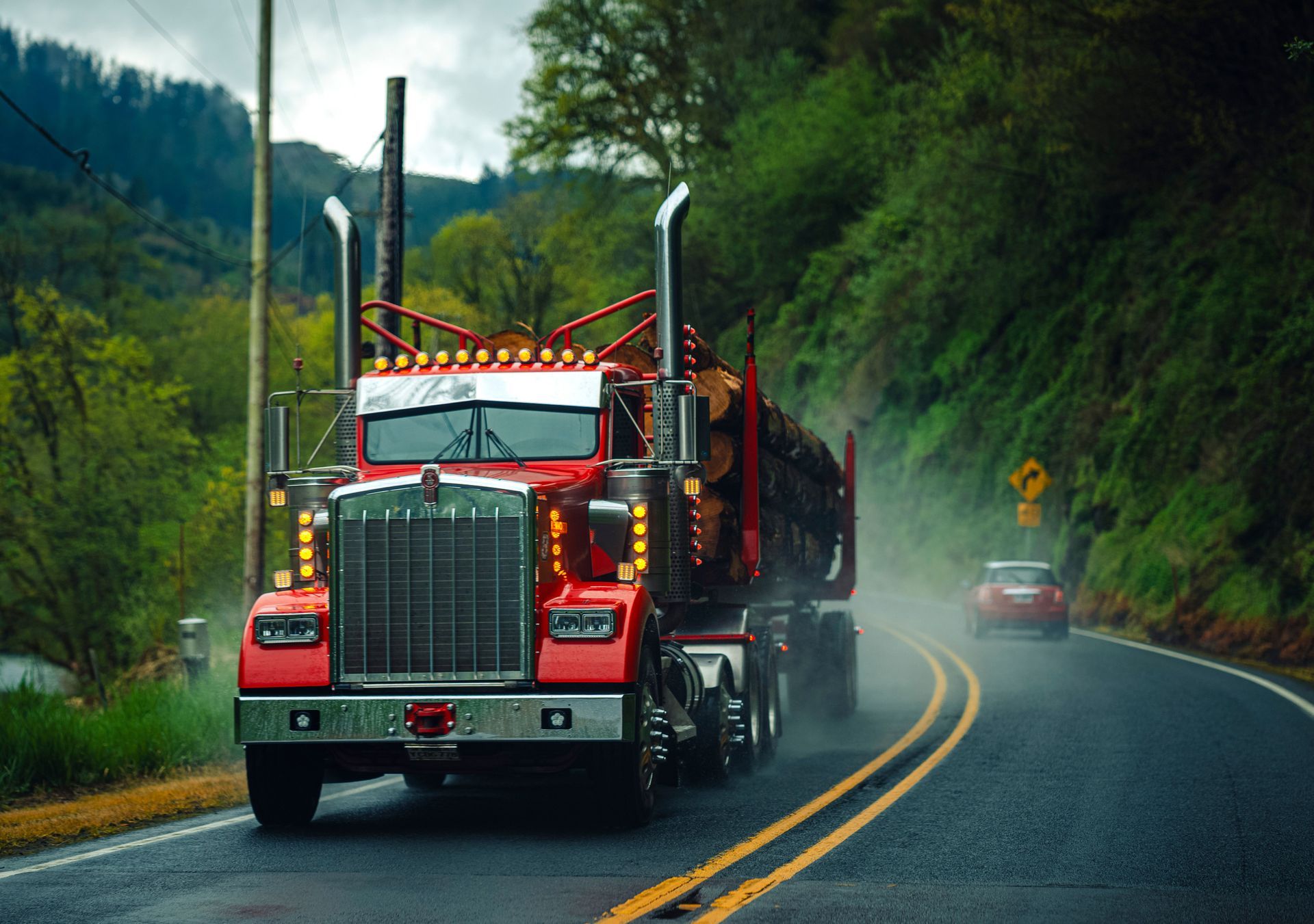 Red semi-truck driving on a wet winding road through a green forest