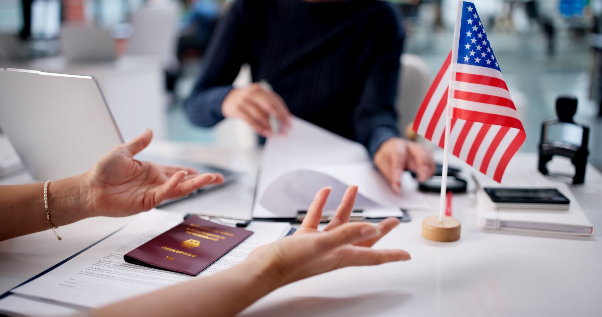 Immigration attorney Elizabeth reviewing visa papers with client and US flag on desk. Immigration attorney Elizabeth reviewing visa papers with client and US flag on desk.