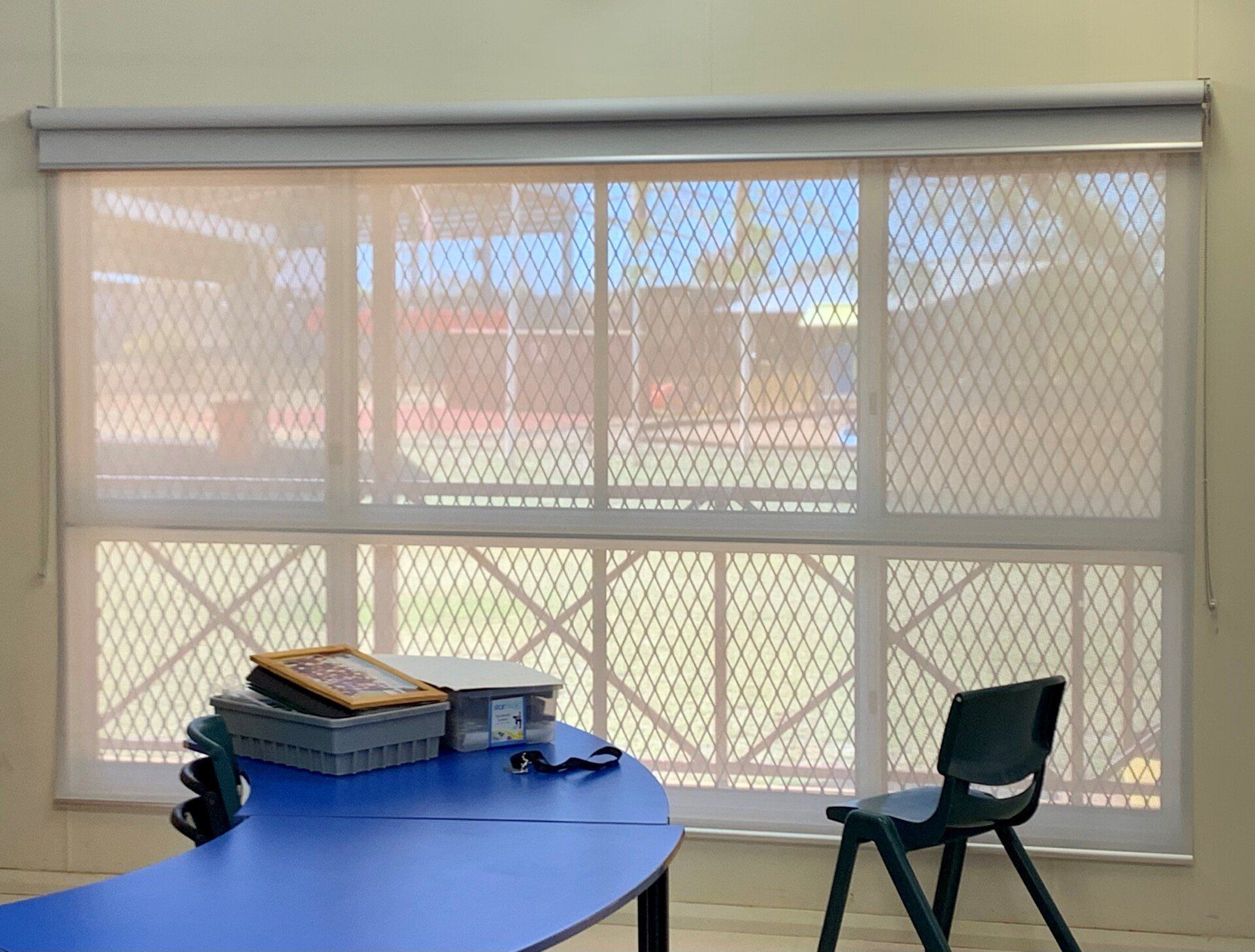 A Classroom Window with A Mesh Screen Blue Table with Items on It — Alice Mobile Blinds in Ciccone, NT