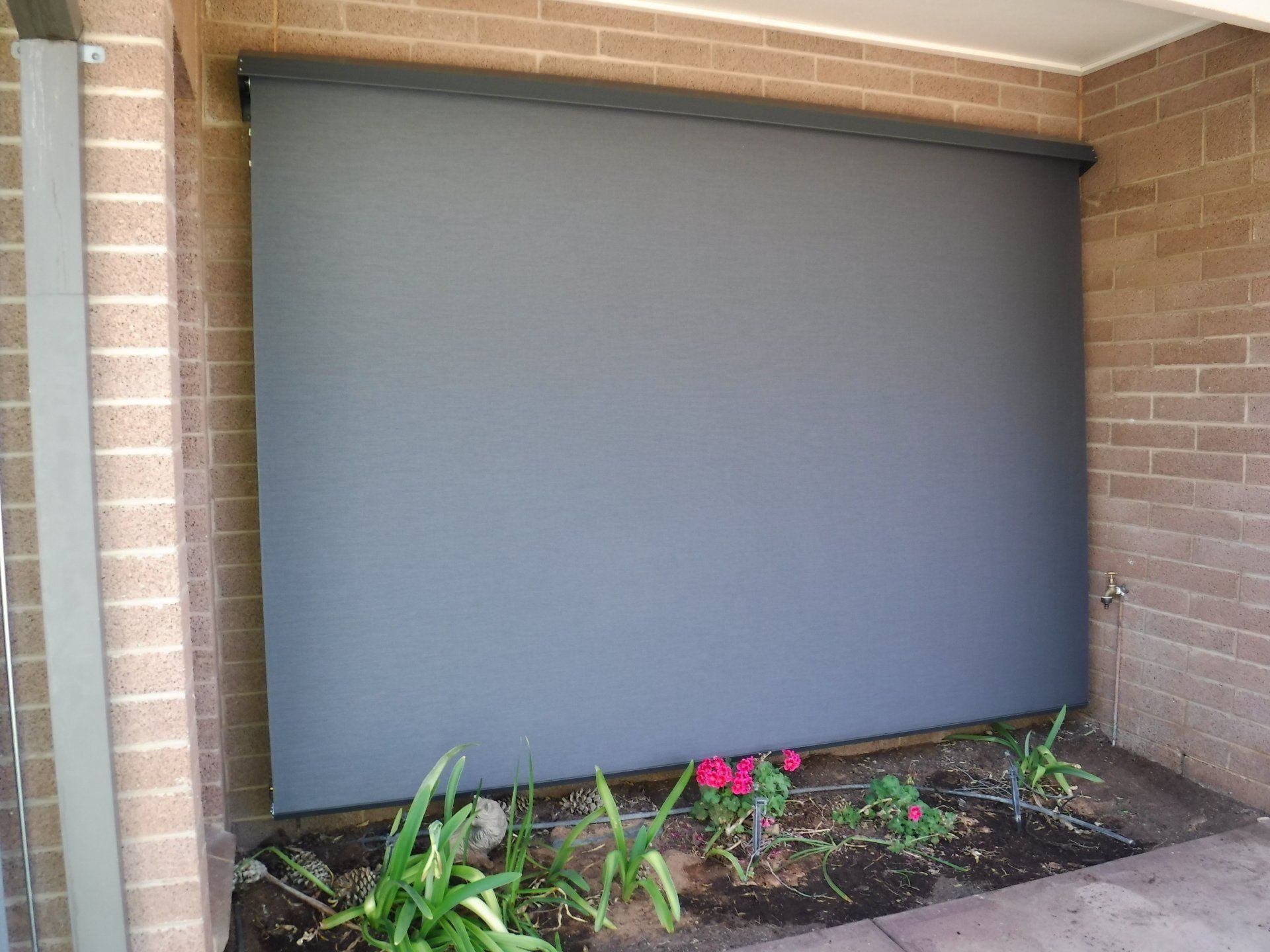 Grey Outdoor Roller Blind Covering a Brick Wall — Alice Mobile Blinds in Ciccone, NT
