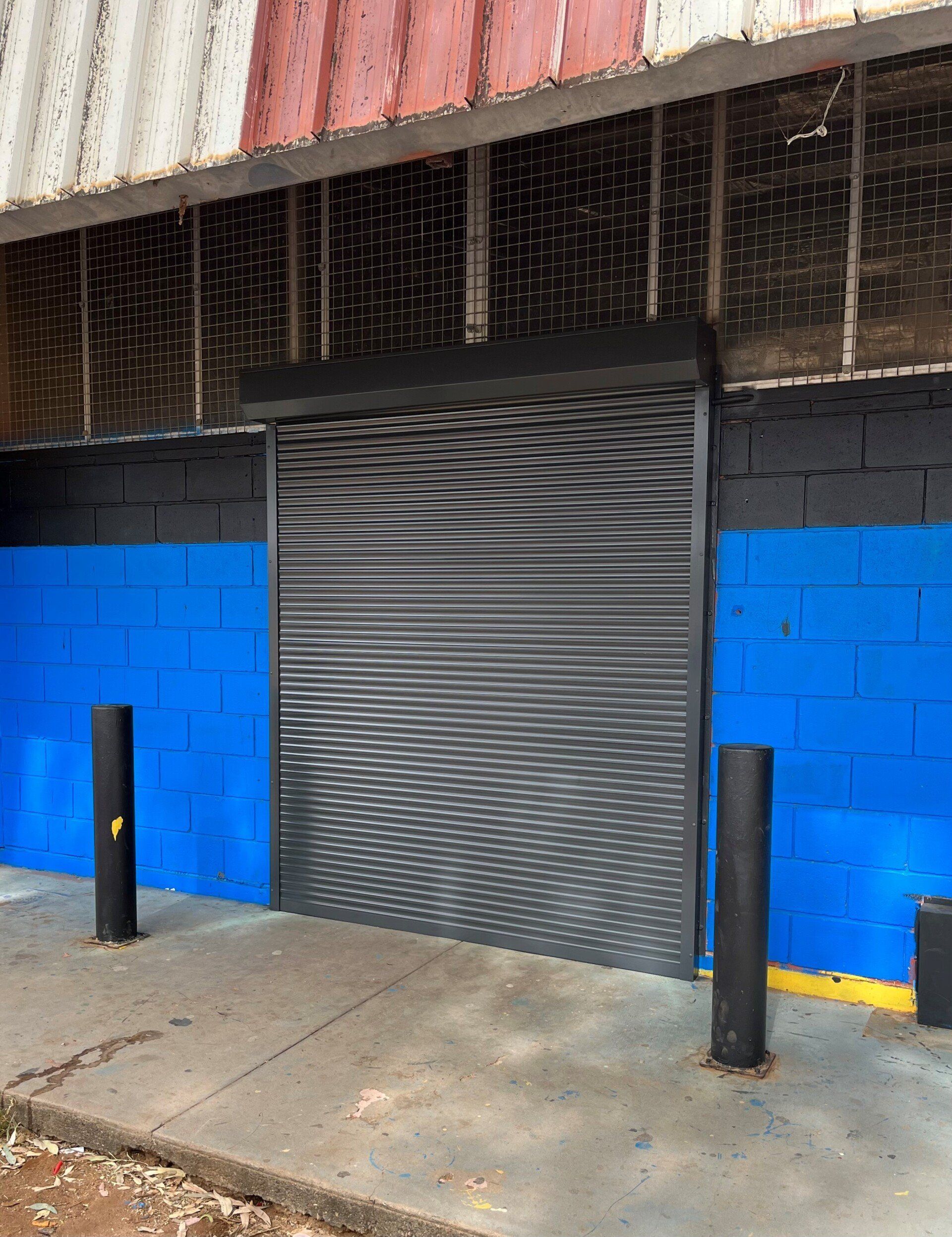 Roller Door in A Building Facade with Black and Blue Walls — Alice Mobile Blinds in Ciccone, NT