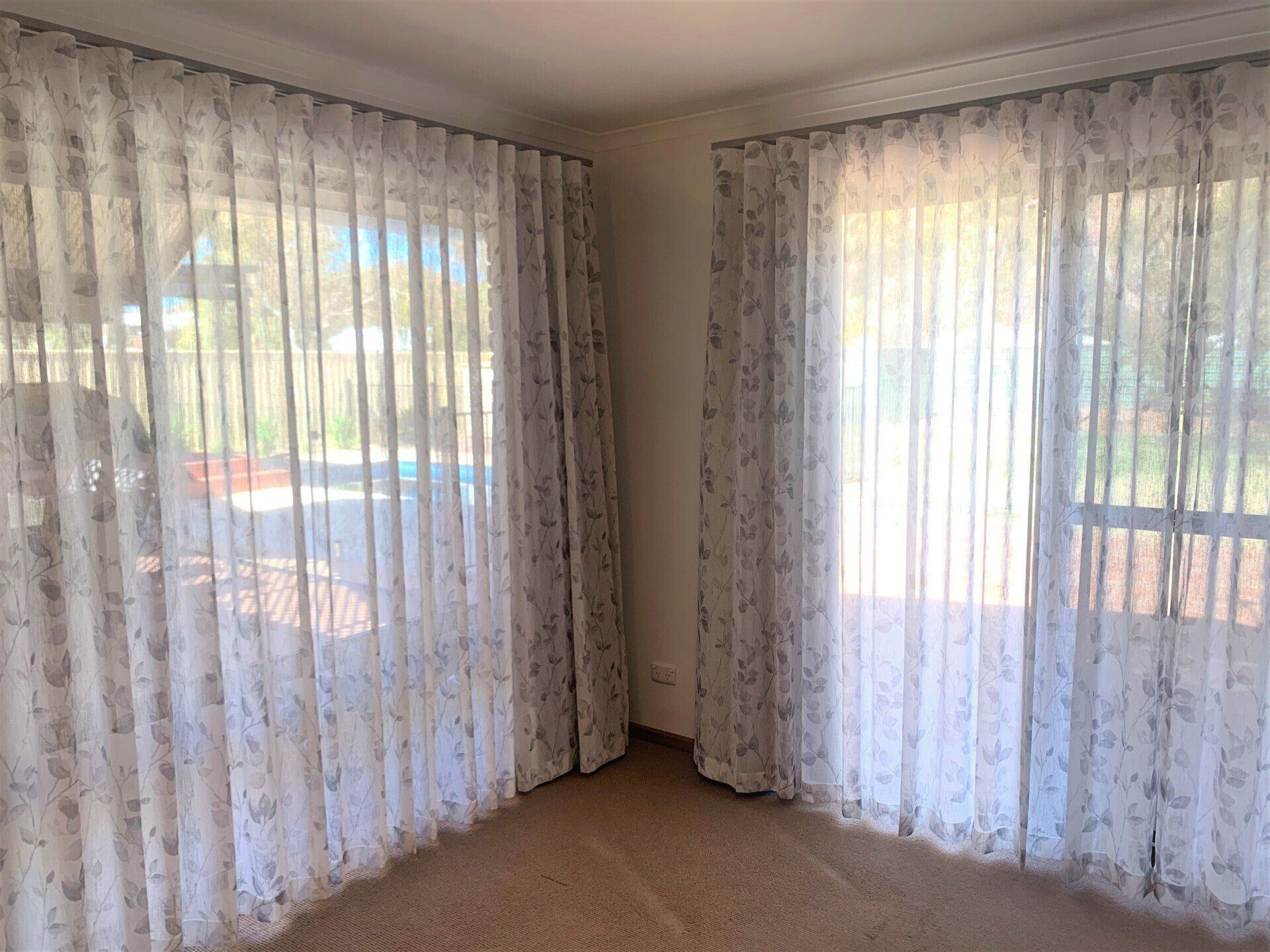 Two Large Windows with Sheer Floral Patterned Curtains — Alice Mobile Blinds in Ciccone, NT