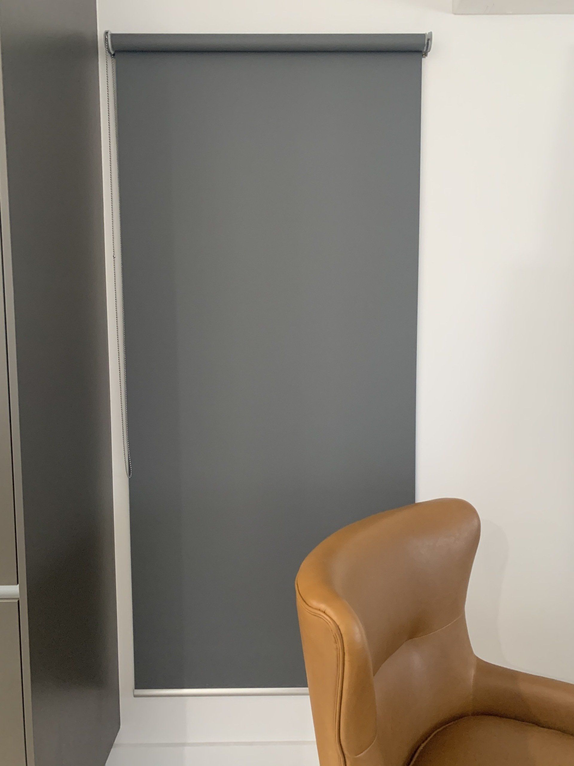 Grey Roller Shade on A Window Next to A Brown Leather Chair — Alice Mobile Blinds in Ciccone, NT