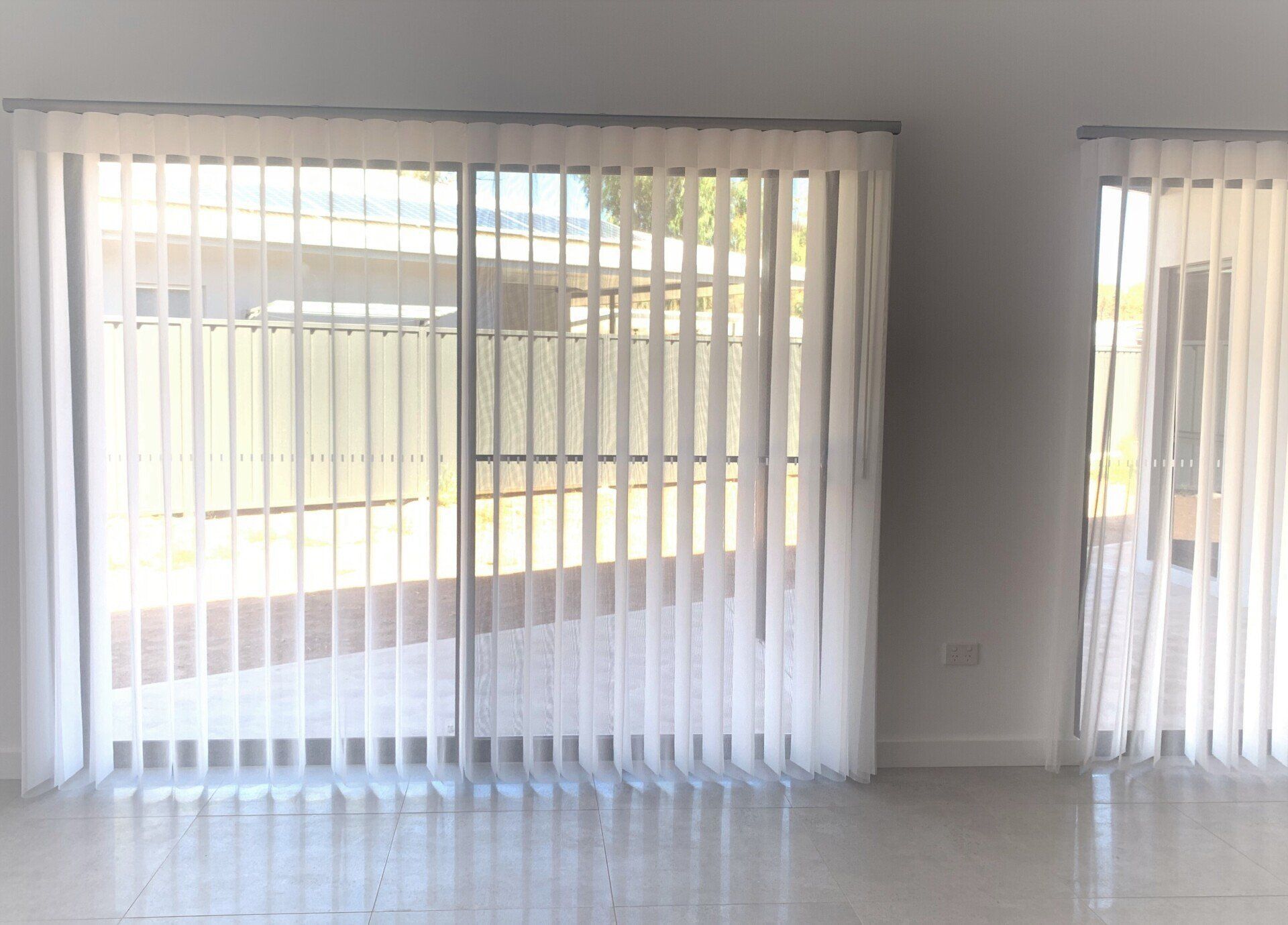 Large Window with White Vertical Blinds Open to A Fenced Yard — Alice Mobile Blinds in Ciccone, NT
