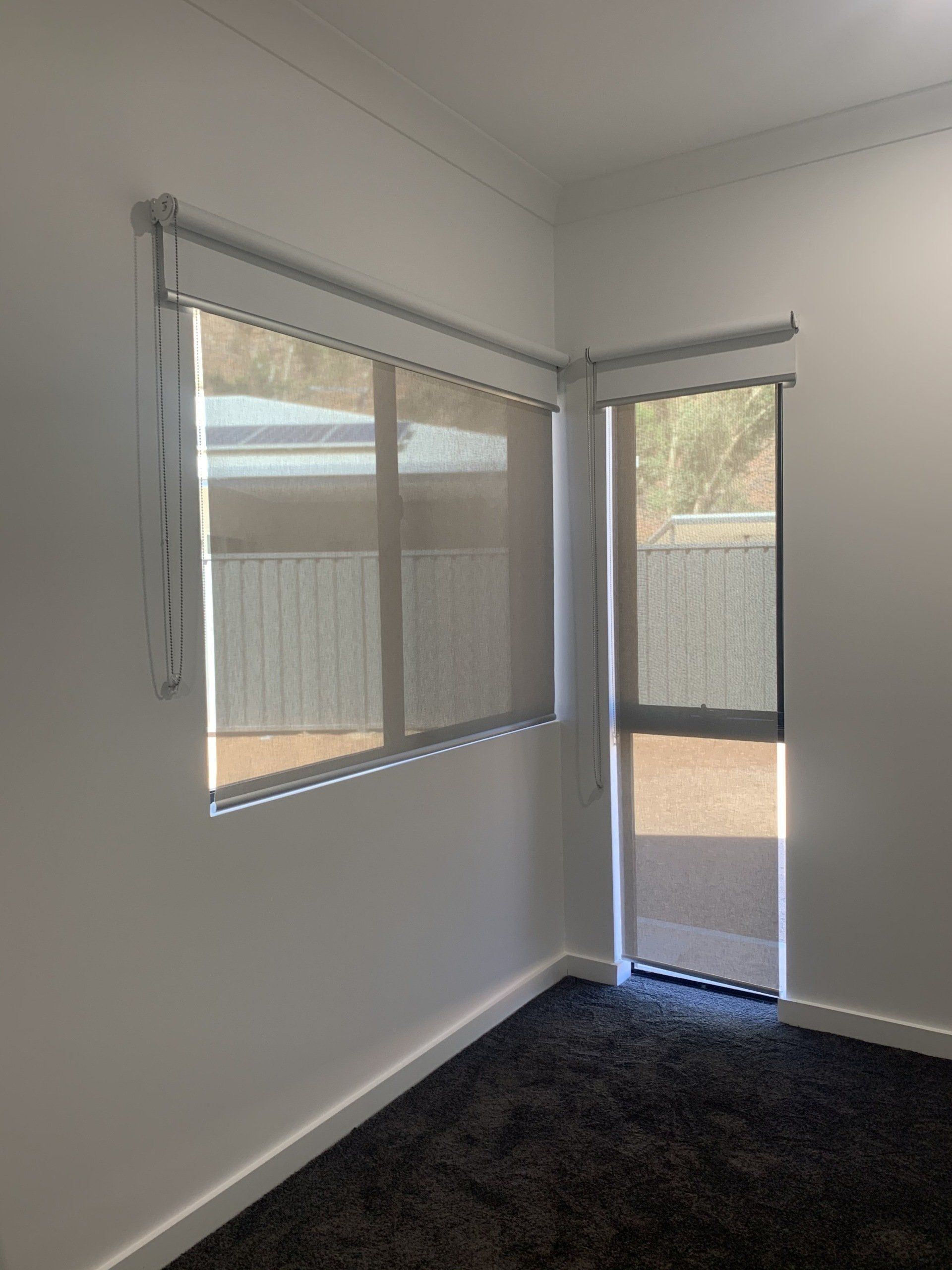 Corner Room with Light Grey Roller Blinds Over Window and Door — Alice Mobile Blinds in Ciccone, NT