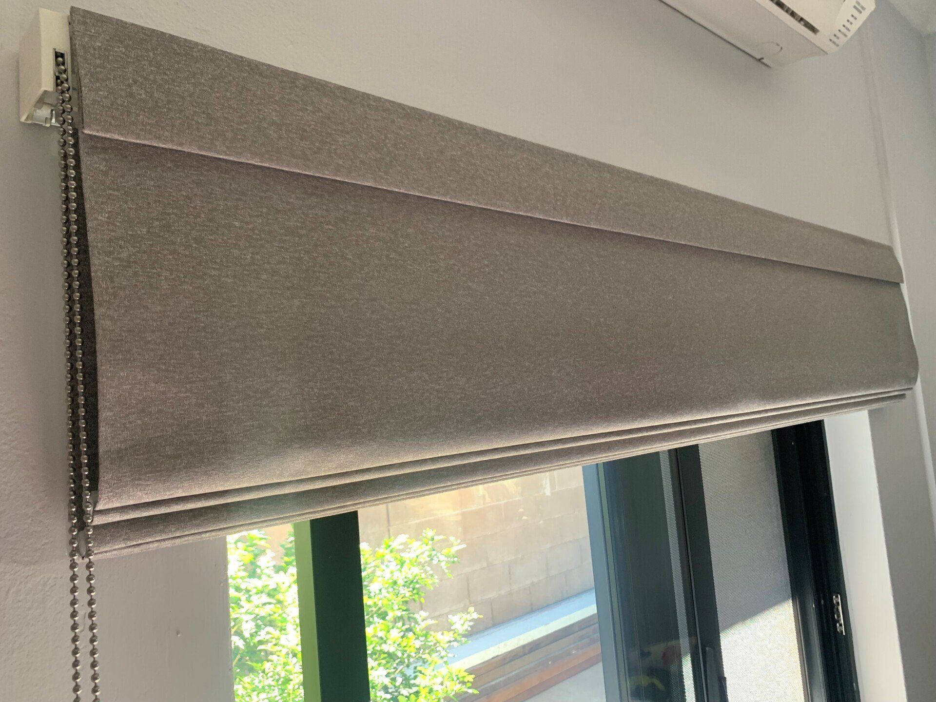 Grey Roman Shade Over a Window Partially Covering the View — Alice Mobile Blinds in Ciccone, NT