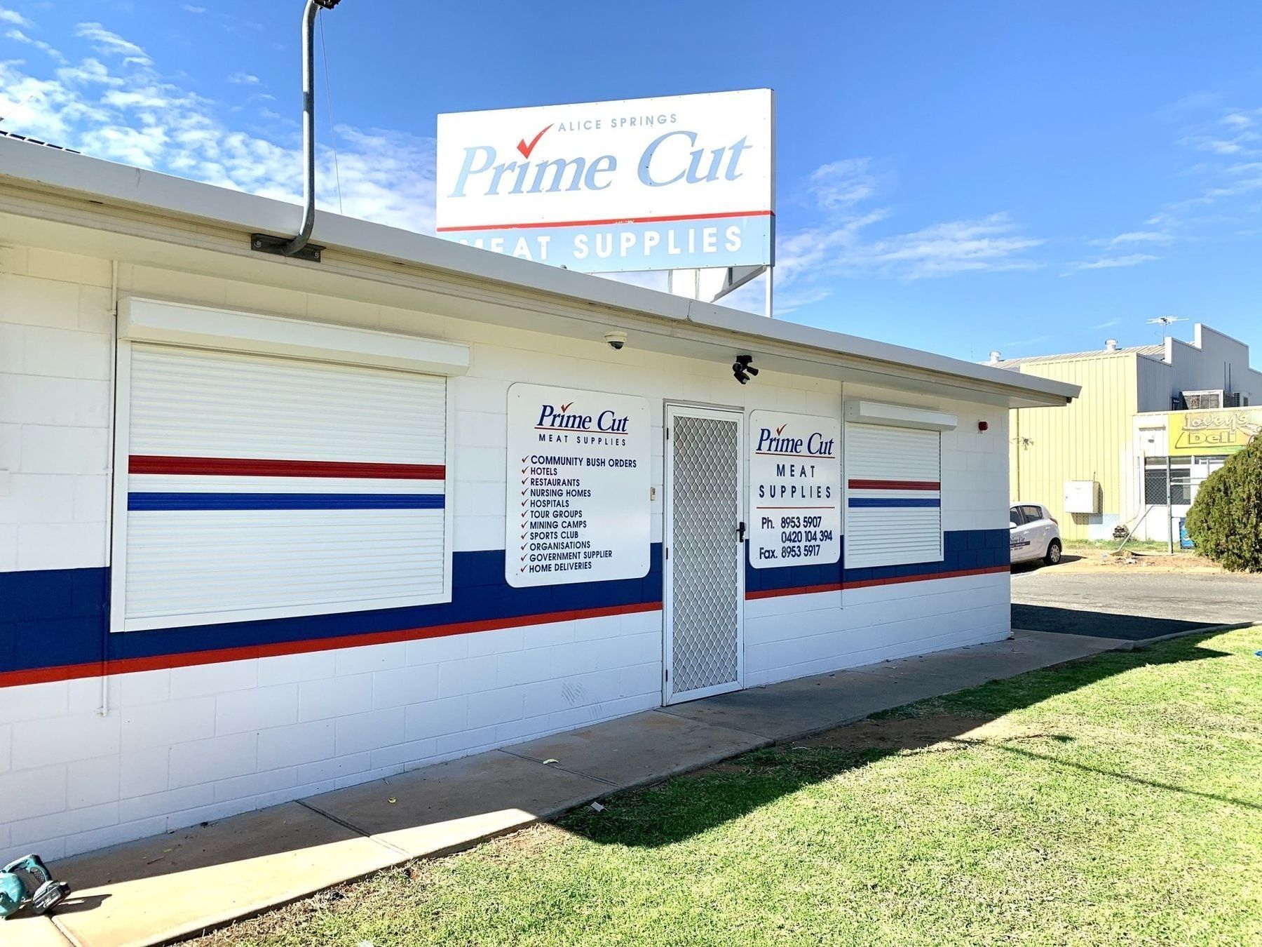 Exterior of Prime Cut Meat Supplies with closed shutters, blue/red accents, and sign. — Alice Mobile Blinds in Ciccone, NT