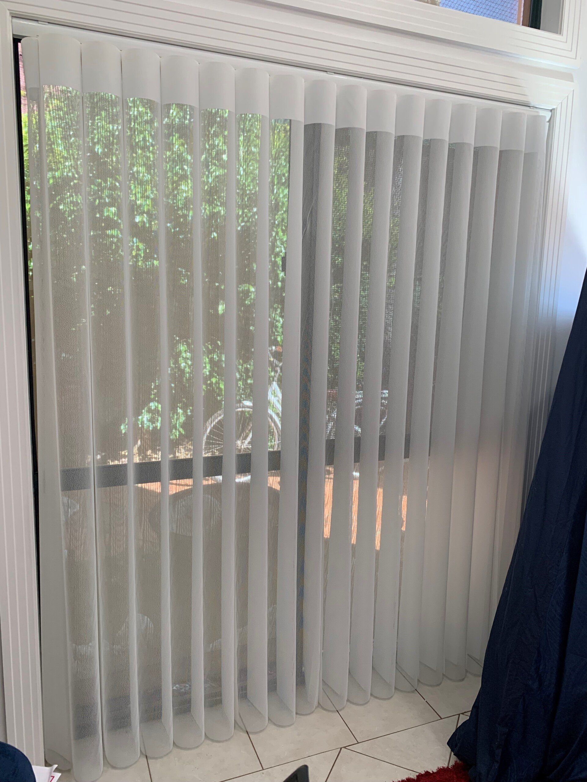 White Vertical Blinds Covering a Window with Greenery Visible — Alice Mobile Blinds in Ciccone, NT