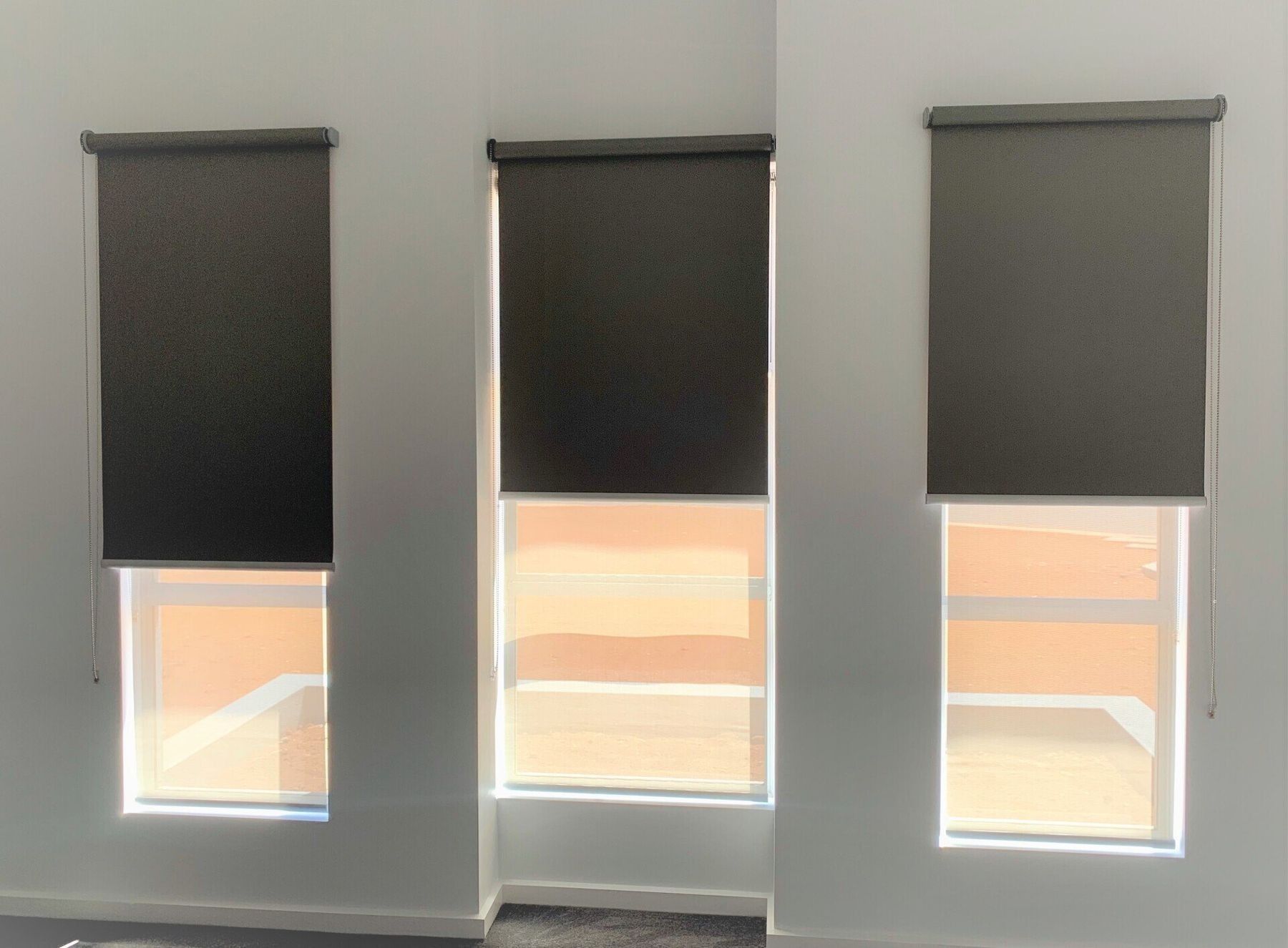 Three Windows with Dark Grey Roller Shades Partially Drawn — Alice Mobile Blinds in Ciccone, NT