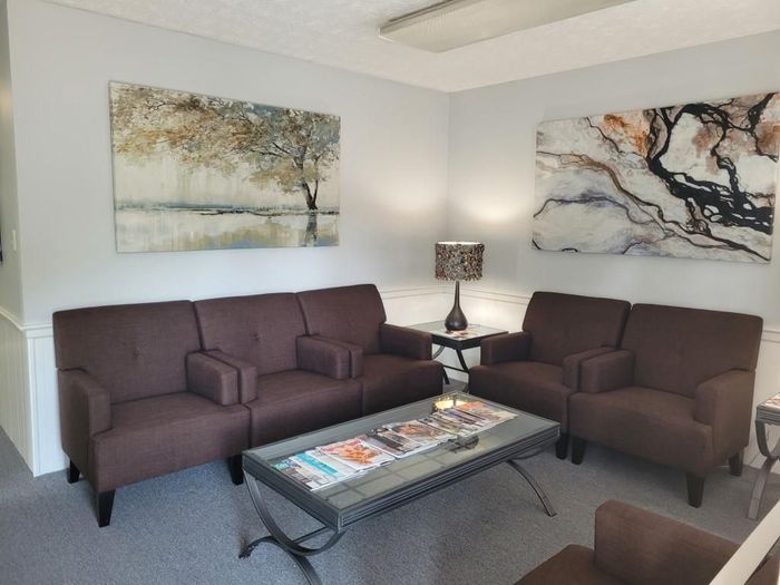 A waiting room with a couch , chairs , and a coffee table.