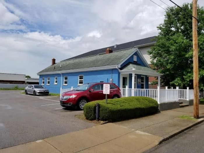 A red car is parked in front of a blue building.